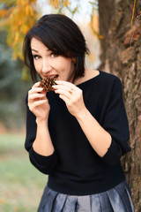 Beautiful elegant woman having fun and eating fir cone in a city park in autumn