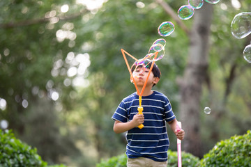Little Chinese boy blowing bubbles on grass