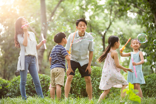 Happy young Chinese family blowing bubbles on grass