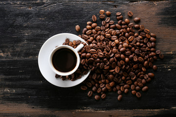 Coffee cup with roasted brown beans scattered on wood textured table with a lot copy space for text. Flat lay composition. Close up, top view, background.