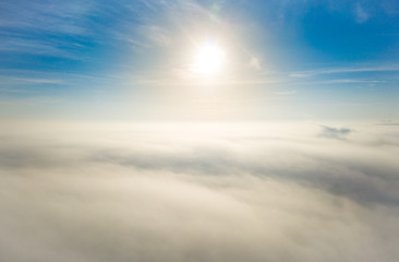 Aerial photo above the fog or white clouds with shining sun. Beautiful sunrise cloudy sky from aerial view. Above clouds from airplane window or drone.