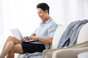 Happy young Chinese man using laptop in living room