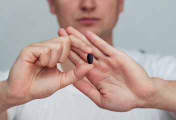 man holds a black pill, closes his mouth with his hand, refusing medicine, protest,