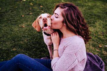 young woman with her dog at the park. she is kissing the dog. autumn season