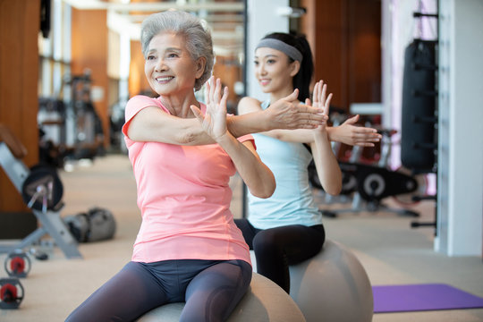 Senior Chinese woman working out with personal trainer at gym