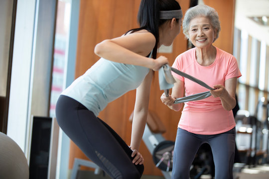 Senior Chinese woman working out with personal trainer at gym