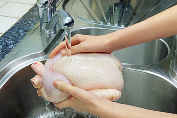 Washing A Fresh Raw Chicken Under Tap Water In The Kitchen Sink.