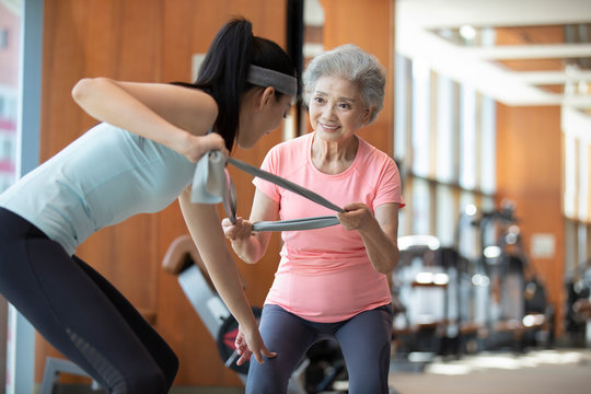 Senior Chinese woman working out with personal trainer at gym