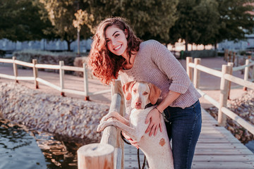 young woman and her dog outdoors walking by a wood bridge in a park with a lake. sunny day, autumn season