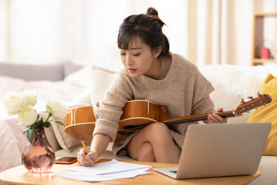 Young Chinese Woman Playing Guitar At Home