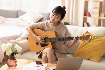 Young Chinese woman playing guitar at home