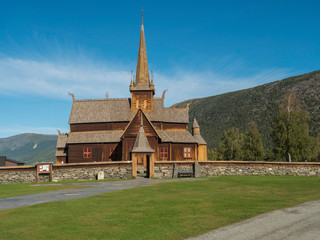 Fototapeta na wymiar Norwegian traditional medieval wooden stave church of Lom also called the post church and palisade , dating from the 12th century, tourist attraction, Norway. Red berries rowan tree and blue sky
