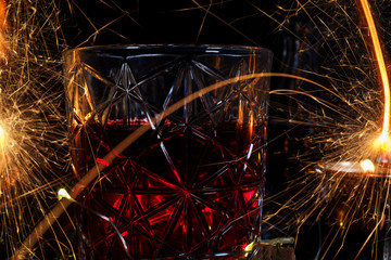 beautiful glass with wine and bright sparks from fireworks, creative photo