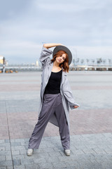 Portrait of beautiful red-haired girl in a grey coat and hat walks around the city