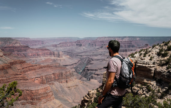 Side view of man with backpack contemplating and standing on mountain top on hot summer day in USA