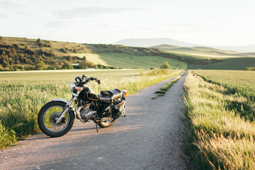 Modern motorbike parked on asphalt road near grassy field on sunny day in peaceful nature