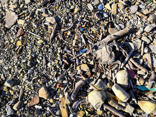 Plastic waste covers and garbage on pebble at seashore after storm, closeup view. Plastic litter garbage waste rubbish on ocean beach. Environmental pollution ecology disaster damage problem.
