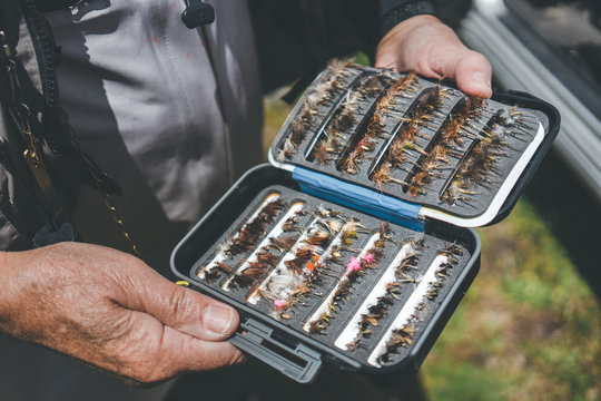 Crop aged man showing arranged lures and hooks while standing on rural street