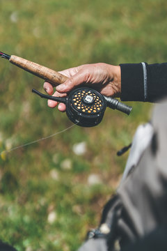 Crop man holding modern fishing tackle while standing at grassy river bank in daylight
