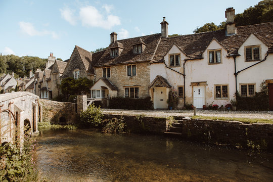 Picturesque view of medieval village Castle Combe with white and gray stone buildings by river in Dorset on sunny day