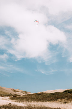 From below people flying with colorful paragliders in cloudy sky near Durdle Door on daytime