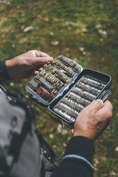 Crop aged man showing arranged lures and hooks while standing on rural street