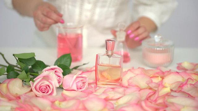 Making body care production beauty aroma perfume roses flowers background on table, Hand of female perfumer lab technician chemist cosmetician pouring cosmetic aroma glass test tube oil in liquid, 4 K