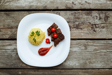 Restaurant food. Pure potatoes combined with grilled pork, decorated with cherry tomatoes. On the wooden floor.