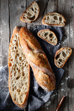 From above whole and halved appetizing baguettes arranged on white towel against rustic wooden background