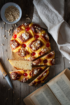 Top view of fresh Coca de San Juan pastry with seeds and open recipe book placed on timber table near towel and knife in rustic kitchen