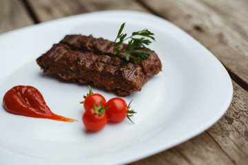 Food in the restaurant. Grilled pork with cherry tomatoes. White plate on a wooden bottom.