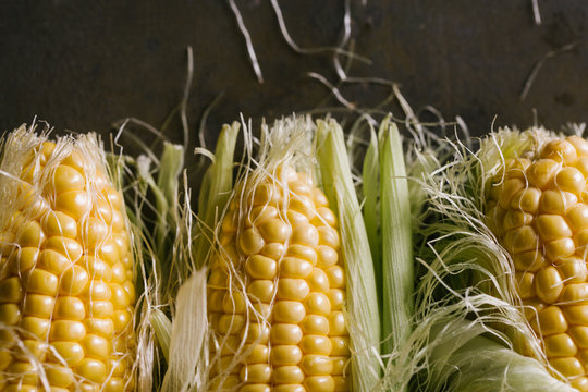Top view of steps of fresh ripe corn peeling on black table