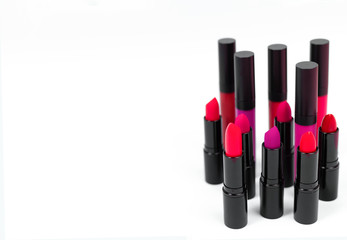 A set of cosmetics for makeup of lipsticks and lip glosses in pink and red colors on a white background whis copy space for text