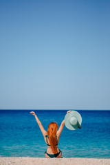 Happy woman enthusiastically raises her hands up sitting on beach