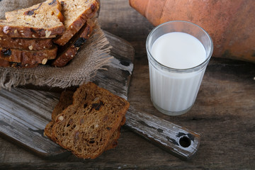 A glass of fresh milk, pieces of rye whole grain bread with prunes and dried apricots and a clay...
