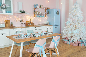 Interior of modern white kitchen with pink walls and blue decor on a Christmas New year eve. Pine tree with wrapped gifts and lights