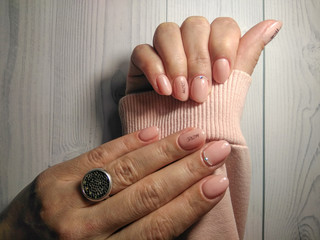 Delicate pink manicure on women's hands in a pink sweater. Gel lacquer pastel peach color with...