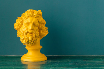 Yellow male head with beard and long hair of the ancient sculpture on a floor against blue wall background