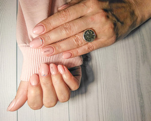 Obraz premium Delicate pink manicure on women's hands in a pink sweater. Gel lacquer pastel peach color with rhinestones design and the inscription 