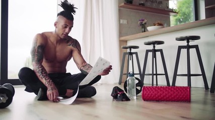 A mixed race young man doing exercise indoors at home, keeping records.