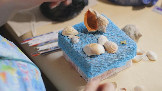 Female artist is making a design on the top cover blue paper box with sea shells