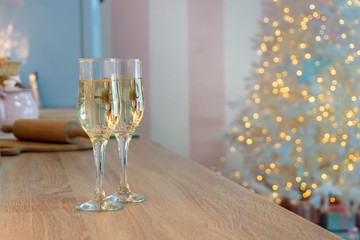Two glasses of champagne on a kitchen. Christmas New year background and decoration, light bokeh effect and light garland