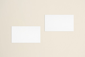 Two empty standard sized white business cards template on bone coloured background. Flat lay, top view. Uneven, open composition. For branding identity, logo design pitches and marketing.