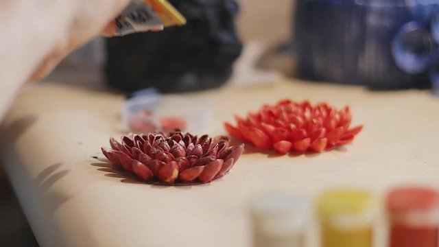 Female artist is making a design of decorative flowers with painted nut shells