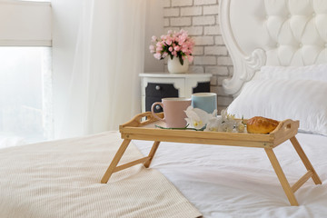 Closeup of Two mugs on a tray with croissant and orchid flower on white luxury bed.Breakfast concept