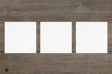 Three empty square white business cards template on wooden background. Flat lay, top view. Open composition. For branding identity, logo design pitches and marketing.
