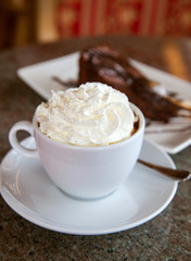Cup of hot chocolate with whipped cream and a piece of cake