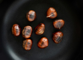 Obraz premium Chestnut on a black frying pan, top view. Roasted Chestnuts close up