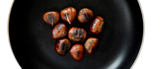 Chestnut on a black frying pan isolated on white background, top view. Roasted Chestnuts close up
