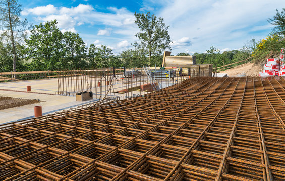 Reinforcing bars grid for ferroconcrete. Building foundations in green trees. Rebar mesh of rusty steel wires for reinforced concrete and masonry on construction site under blue sky with white clouds.